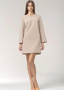 Isang maikling 60-inspired na murang beige na damit na may mahabang sleeves at isang pares ng mga sapatos na pangbabae.